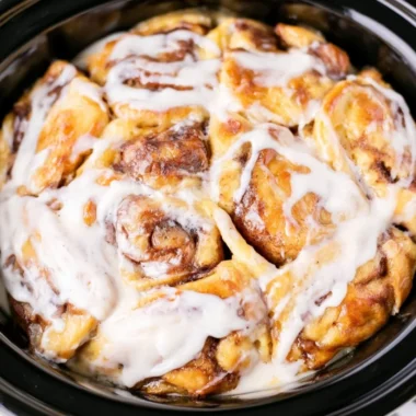 Crockpot cinnamon roll casserole topped with icing and served in a bowl