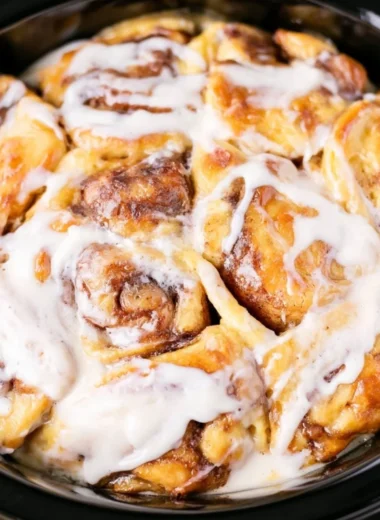 Crockpot cinnamon roll casserole topped with icing and served in a bowl