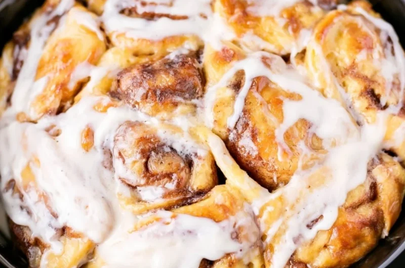 Crockpot cinnamon roll casserole topped with icing and served in a bowl