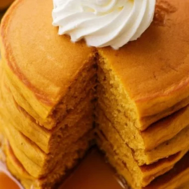 Fluffy pumpkin pancakes drizzled with syrup and topped with whipped cream.