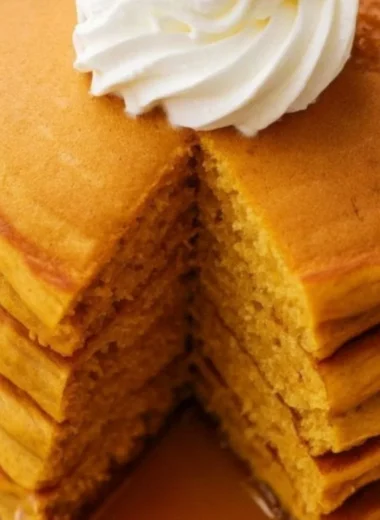 Fluffy pumpkin pancakes drizzled with syrup and topped with whipped cream.