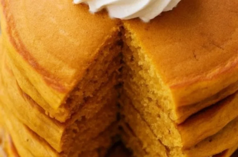 Fluffy pumpkin pancakes drizzled with syrup and topped with whipped cream.