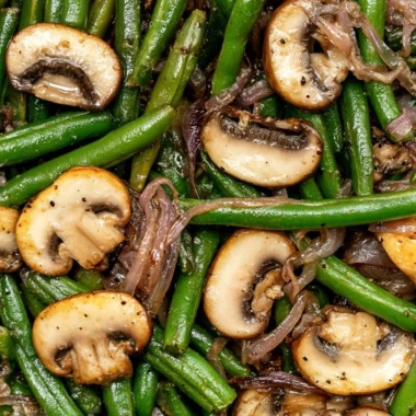 Sautéed green beans with mushrooms in a skillet, garnished with herbs.
